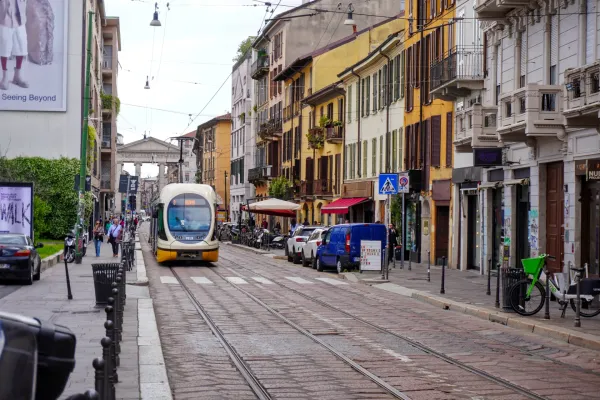 Un tranvía amarillo y blanco circula por una calle de Milán con edificios antiguos y tiendas a los lados.