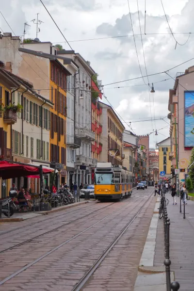Eine Straße in Mailand, Italien, mit Kopfsteinpflaster, Straßenbahnschienen und Gebäuden auf beiden Seiten. Ein Ziegelsteinbogen ist im Hintergrund sichtbar.