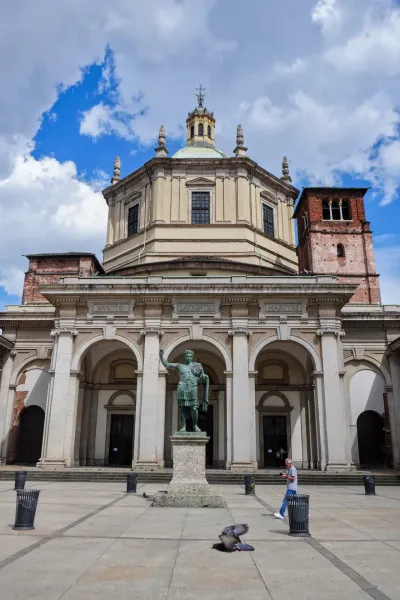 Statue von Kaiser Konstantin vor der Basilica di San Lorenzo Maggiore mit Kuppel und Glockenturm unter einem bewölkten Himmel.