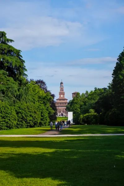 Un sendero a través de un exuberante parque verde en Milán conduce al imponente Castillo Sforzesco con su distintiva torre del reloj.