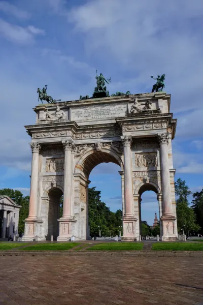 El Arco de la Paz, un gran arco neoclásico, coronado por una escultura de cuadriga bajo un cielo azul brillante con nubes dispersas.