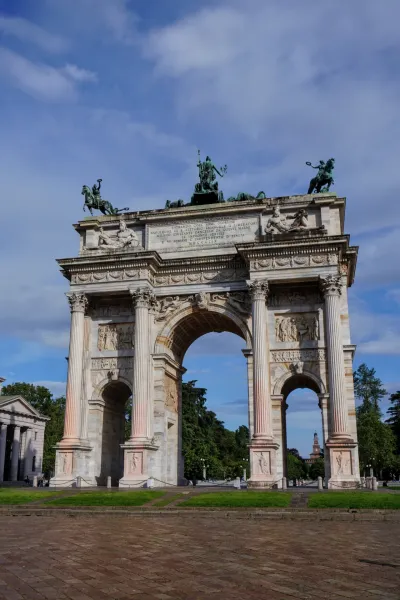 El Arco de la Paz, un gran arco de triunfo neoclásico, se alza contra un cielo azul parcialmente nublado, con árboles y césped en primer plano.
