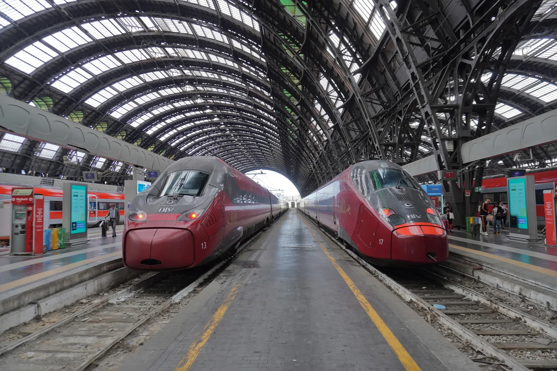 Zwei moderne rote Hochgeschwindigkeitszüge warten auf den Bahnsteigen im Bahnhof Milano Centrale unter seinem großen Bogenglasdach.