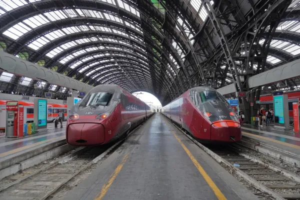 Zwei moderne rote Hochgeschwindigkeitszüge warten auf den Bahnsteigen im Bahnhof Milano Centrale unter seinem großen Bogenglasdach.