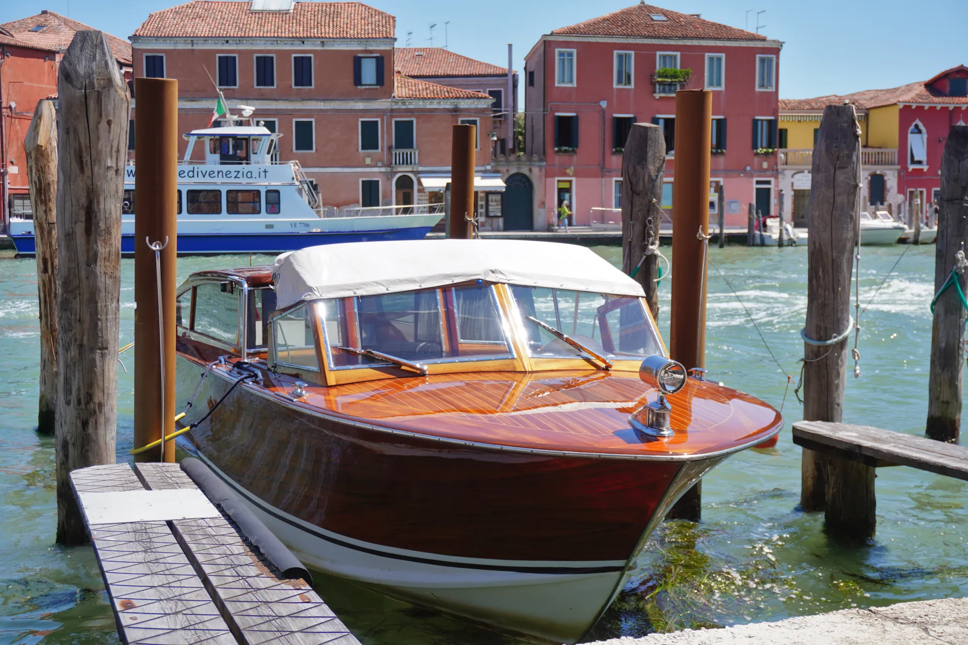 A vintage wooden water taxi is moored in a Venetian canal, with colorful buildings lining the waterfront.