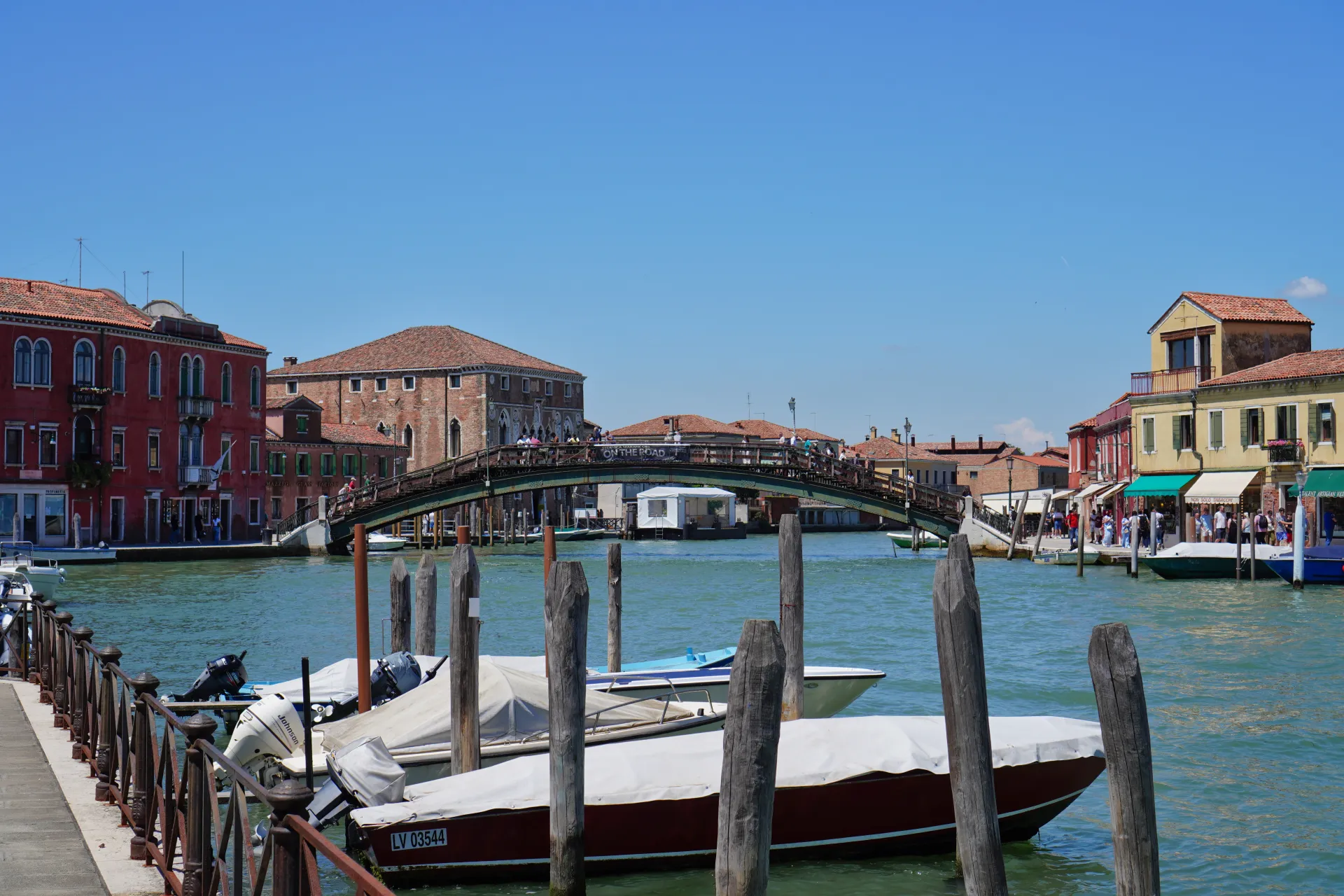 A view of a canal on Murano Island, Venice, Italy, with boats moored and a bridge in the background.