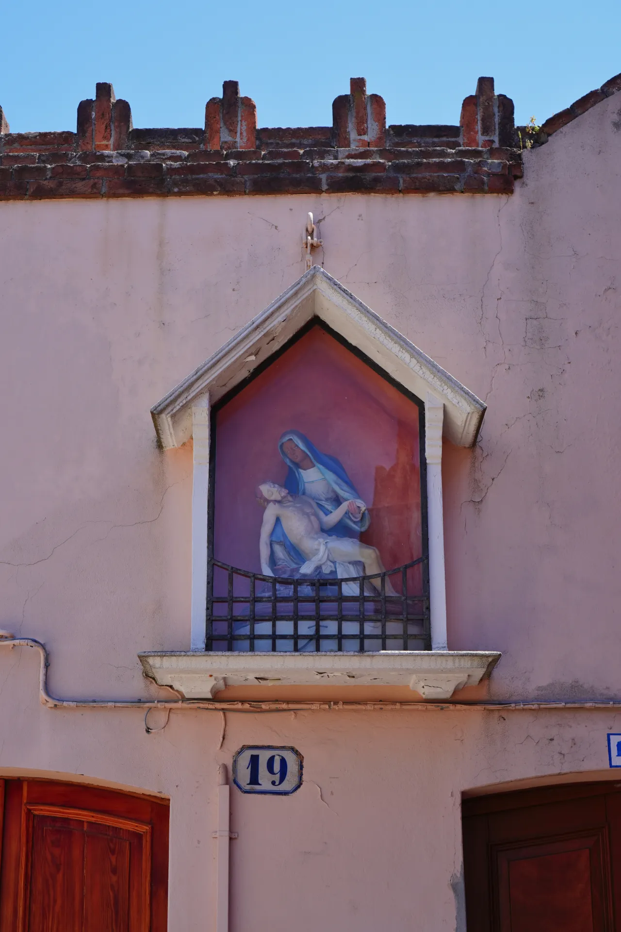 Fresco of the Madonna holding the body of Christ, located on a building on Murano island, Venice, Italy, with the number 19 on the wall.