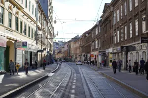 A sunlit street in Zagreb, Croatia, with tram tracks in the middle and buildings on either side, with pedestrians walking on the sidewalks.