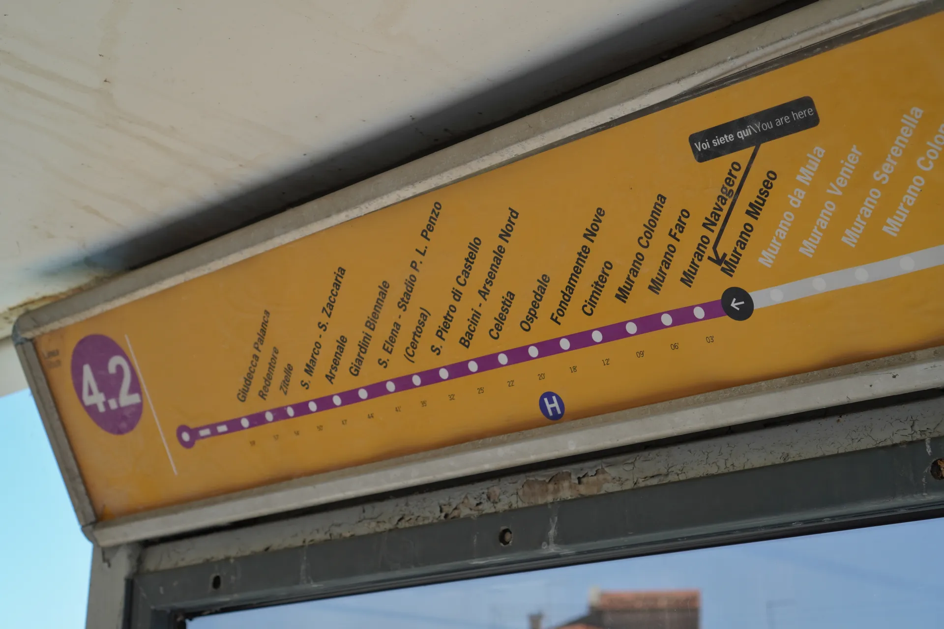 A sign displaying the Vaporetto line 4.2 route map in Venice, Italy, showing various stops with a prominent marker pointing to the Murano Island (остров Мурано) and indicating a теплохода (ship) stop.