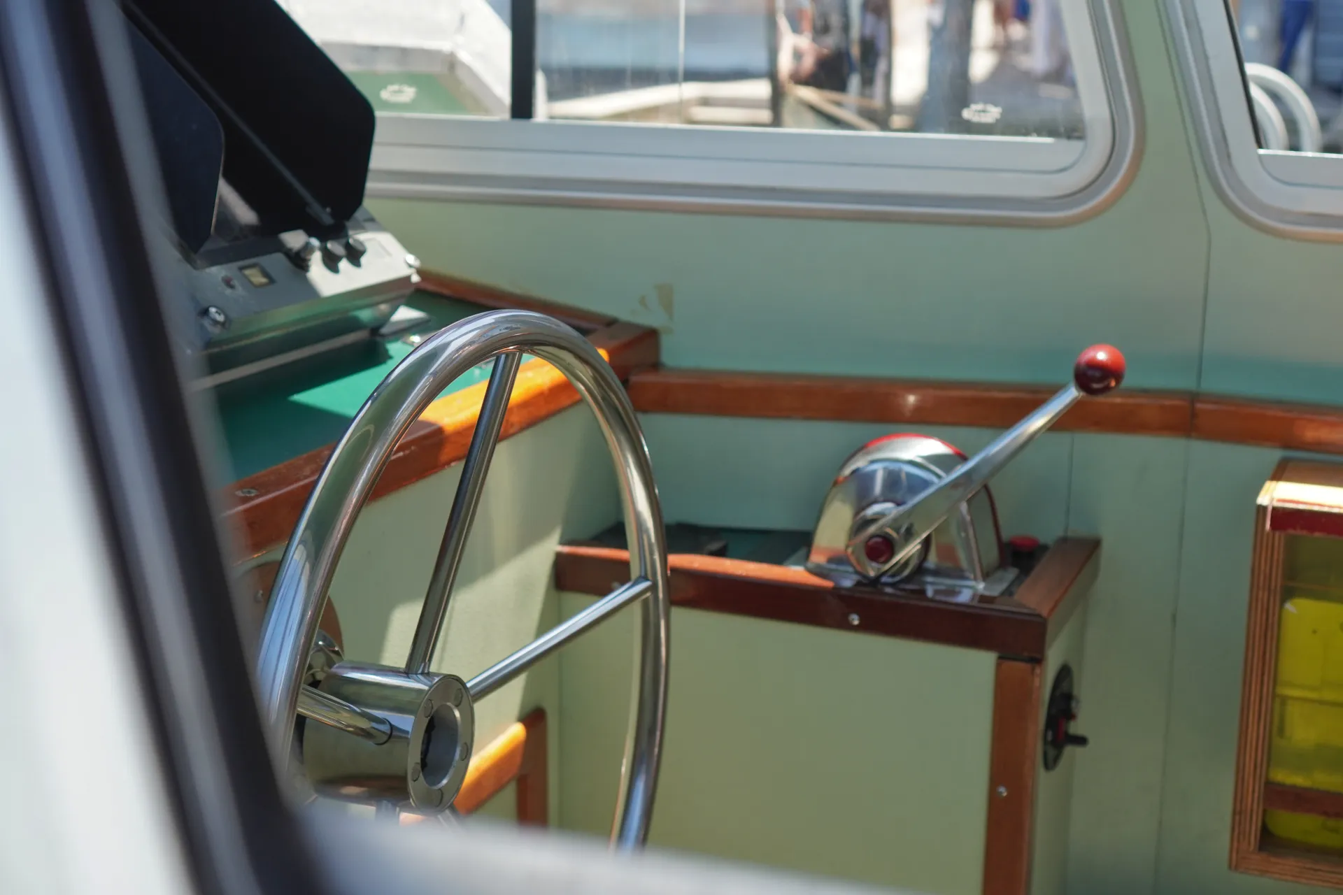 Close-up of a shiny chrome steering wheel (штурвал) inside a Venetian water bus, with throttle controls visible in the background, suggesting travel through Venice, Italy.