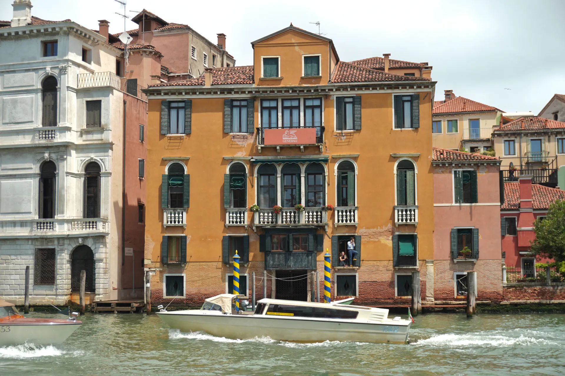 A white water taxi speeds through a canal in Venice, Italy, with traditional colorful buildings lining the waterway.