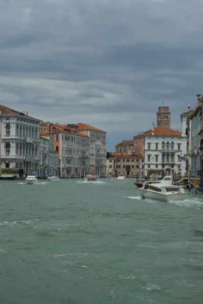 Boote auf dem Canal Grande in Venedig, Italien, mit verzierten Gebäuden und einem Glockenturm im Hintergrund unter einem bewölkten Himmel.