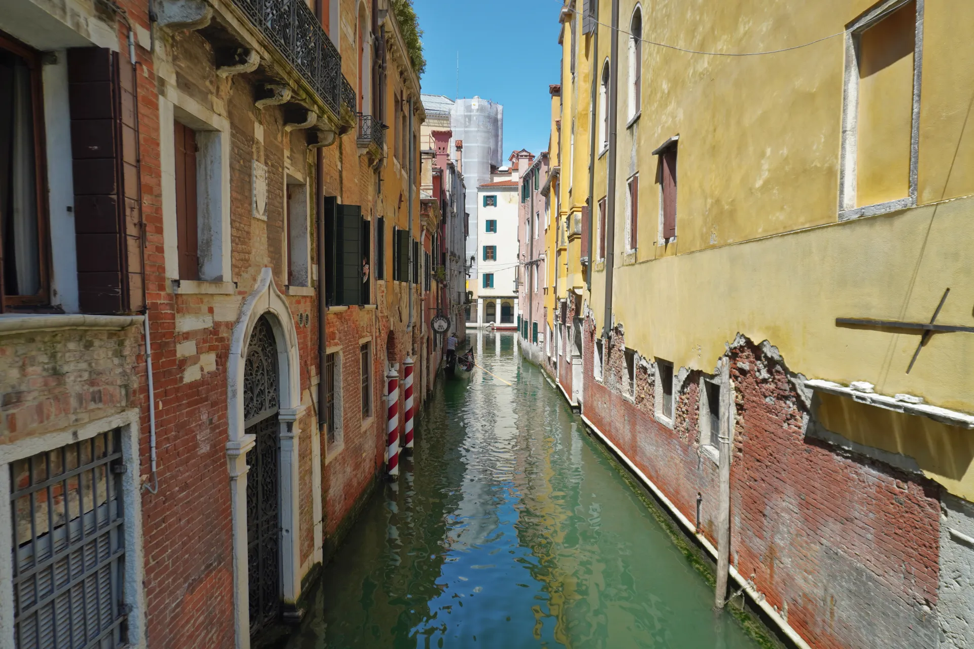 A gondola rows down a narrow canal in Venice, Italy, with colorful buildings on either side and reflections in the water.